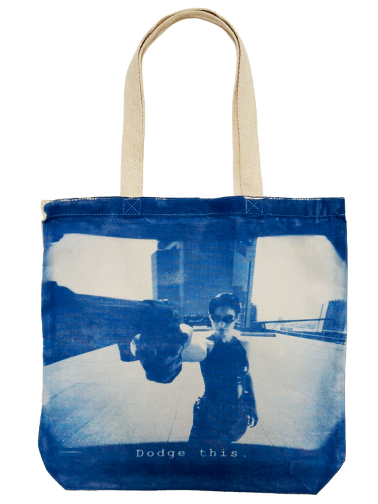 Trinity from The Matrix poiniting at the screen with a gun saying "Dodge This" on a cyanotype print tote bag